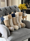 BurlapBabe set of five rustic Christmas stockings featuring burlap and blue ticking fabric on a grey armchair.