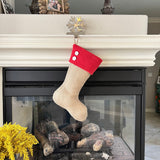 BurlapBabe burlap Christmas stocking with a red fleece cuff and two white wooden buttons hanging on a fireplace mantel