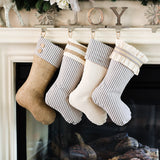BurlapBabe set of four farmhouse Christmas stockings with blue ticking, burlap, and cream muslin hanging on a mantle.