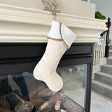 BurlapBabe handmade quilted Christmas stocking in neutral cream with a white cuff hanging on a fireplace mantle.